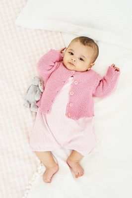 A baby is wearing a pink knitted cardigan.