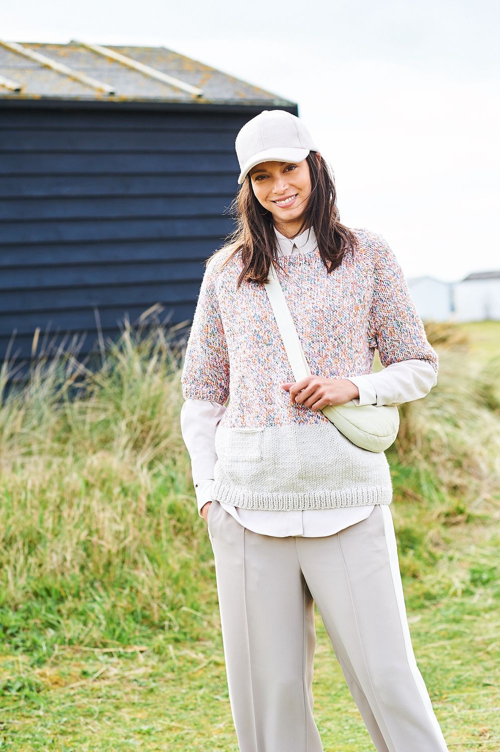 A woman is wearing a knitted sweater, with the top half in a variegated white and rainbow yarn and the bottom half in solid white.