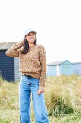 A woman is wearing a knitted sweater in a variegated yellow-brown yarn.