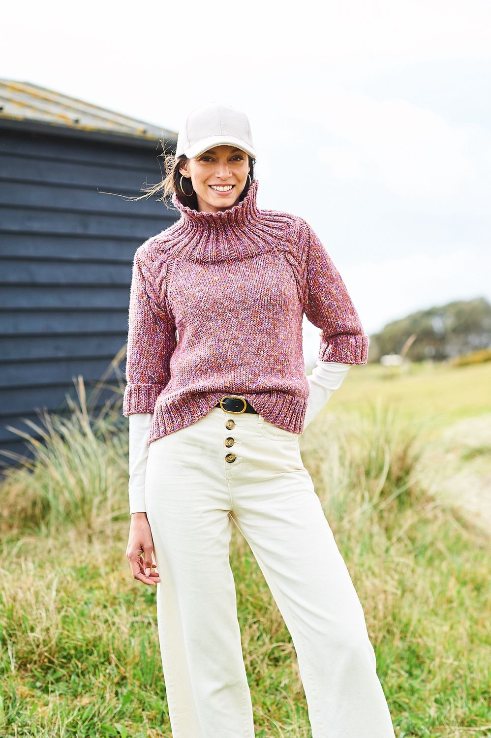 A woman is wearing a knitted sweater in a variegated pink-brown yarn.
