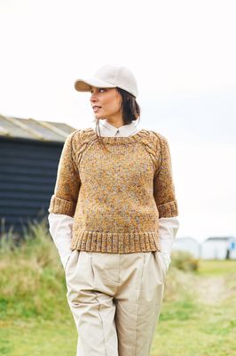 A woman is wearing a knitted sweater in a variegated yellow-brown yarn.