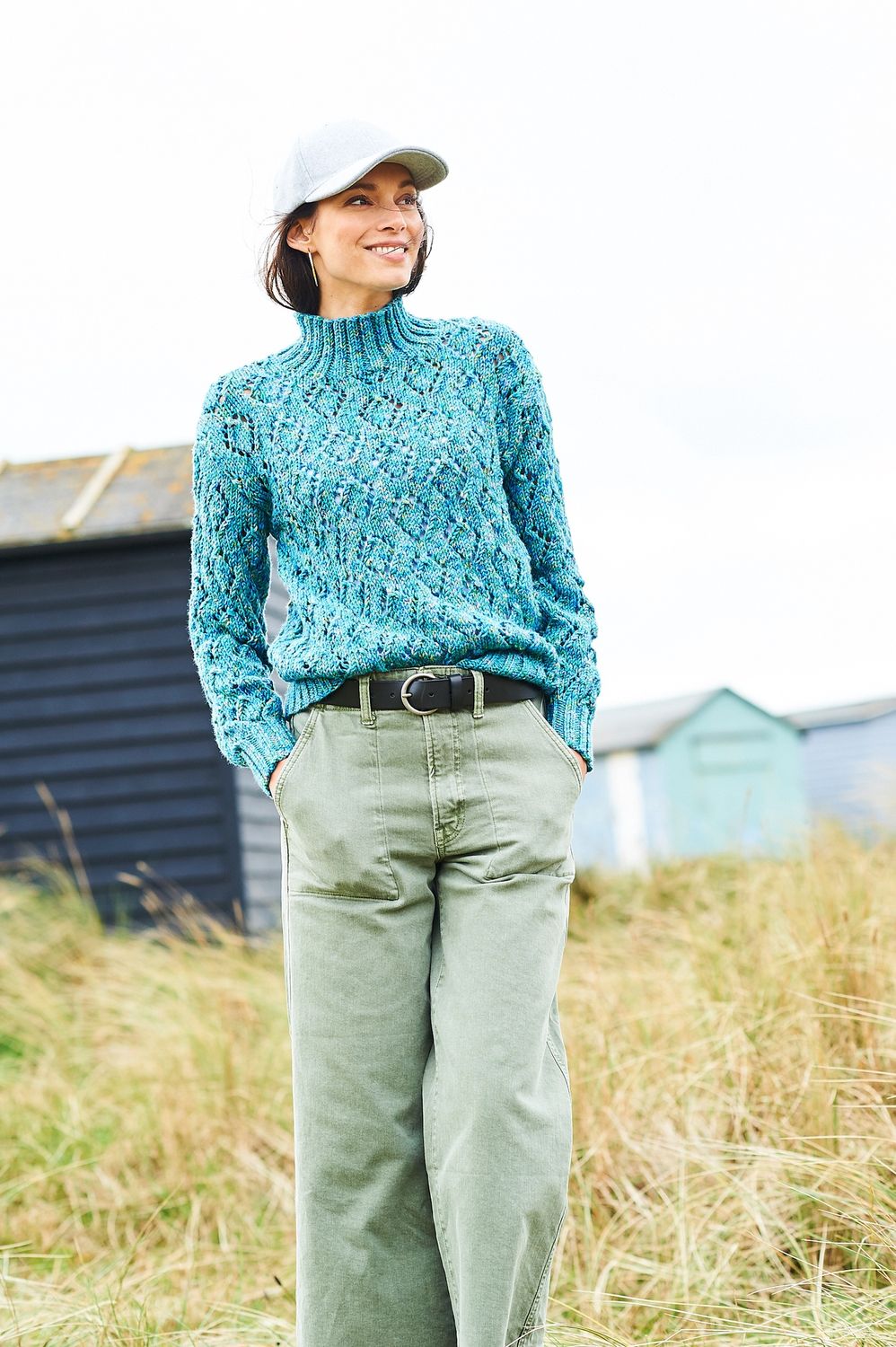 A woman is wearing a knitted sweater in a variegated teal blue yarn.