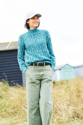 A woman is wearing a knitted sweater in a variegated teal blue yarn.