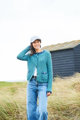 A woman is wearing a knitted jacket in a variegated teal blue yarn.