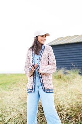 A woman is wearing a knitted cardigan in a variegated white and rainbow yarn.