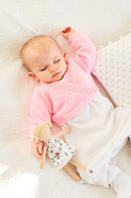 A baby is wearing a pink knitted cardigan.