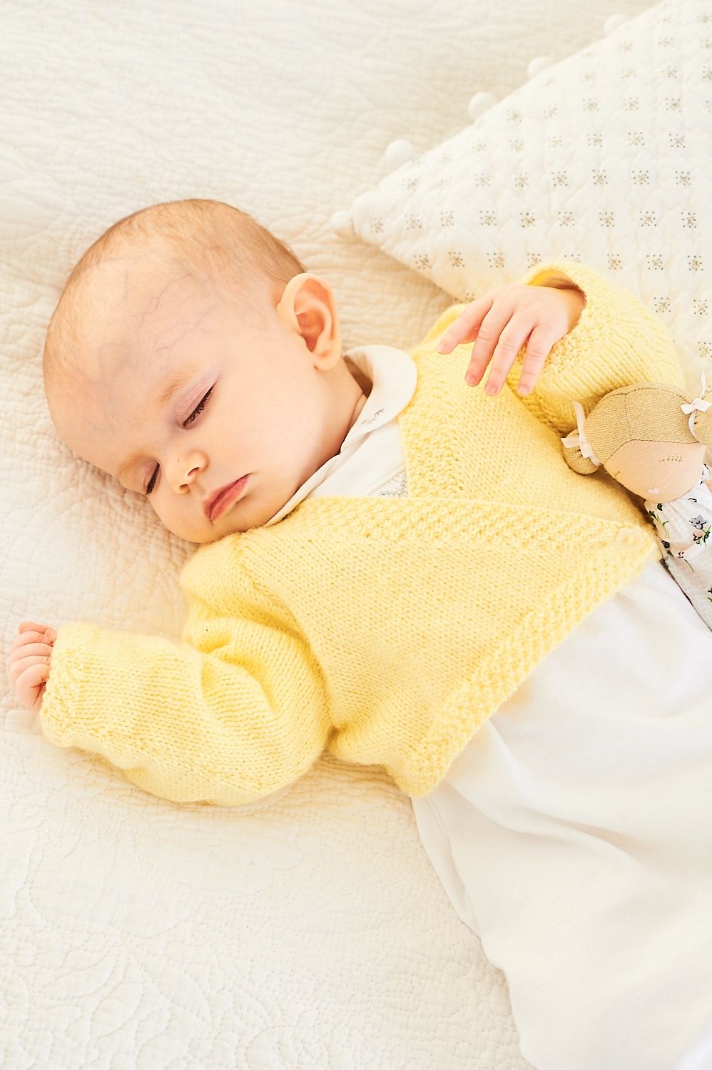 A baby is wearing a yellow knitted cardigan.