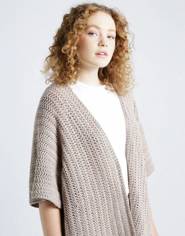 A woman is wearing a beige crocheted cardigan.