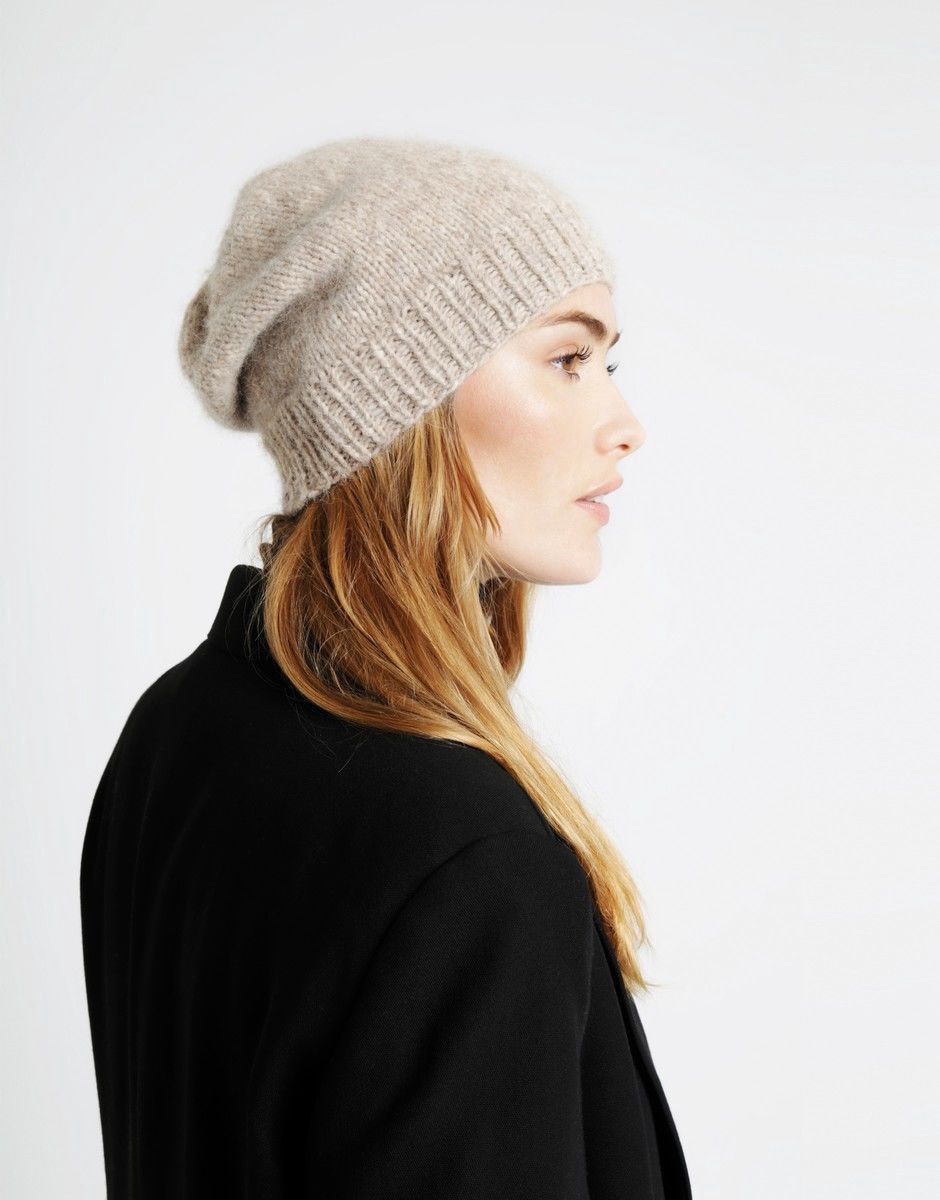 A woman is wearing a pale beige knitted hat.