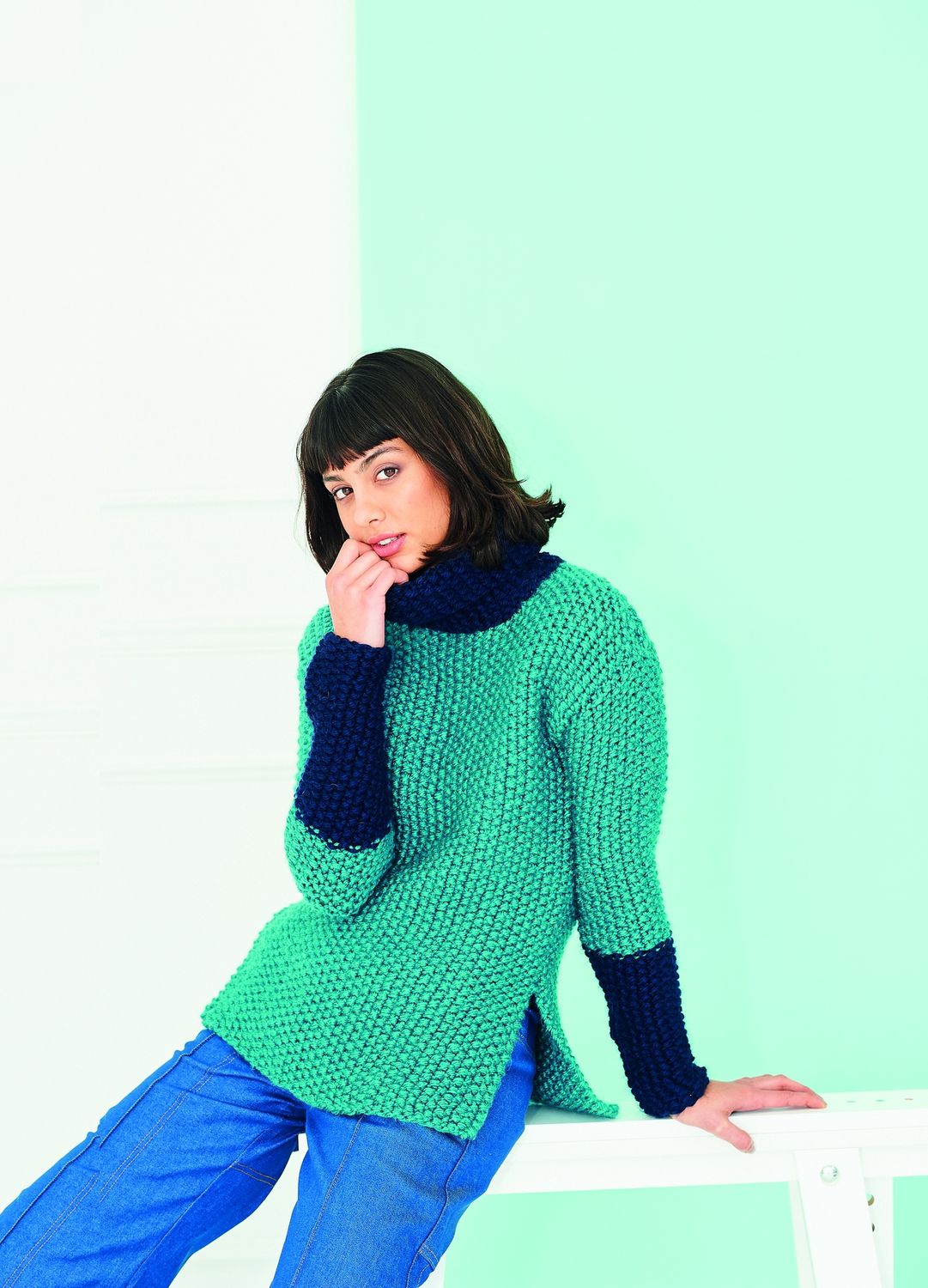 A woman is wearing a teal knitted sweater with navy blue sleeves.