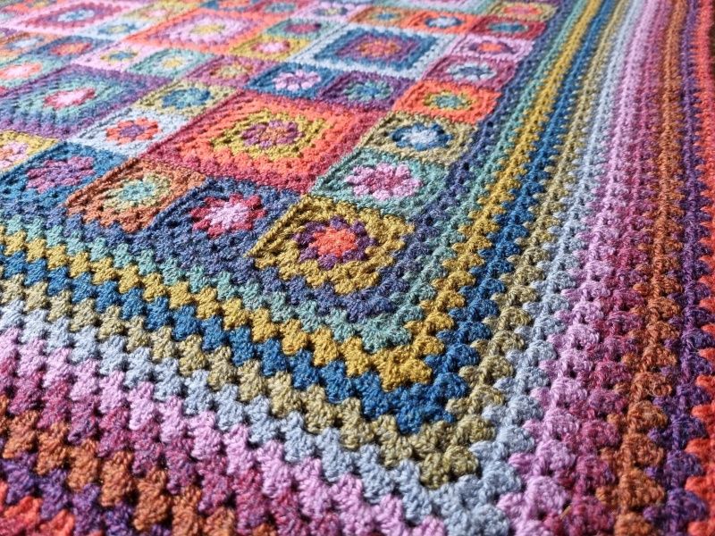 A close up angled view of the blanket in shades of green, orange, blue and pink.