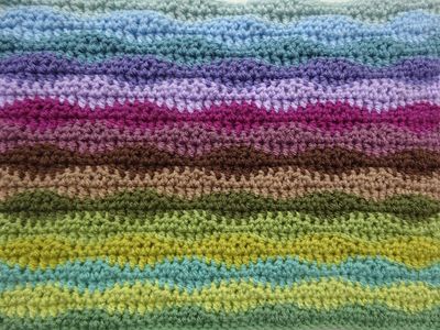 A striped crochet blanket in shades of green, blue, purple and brown.