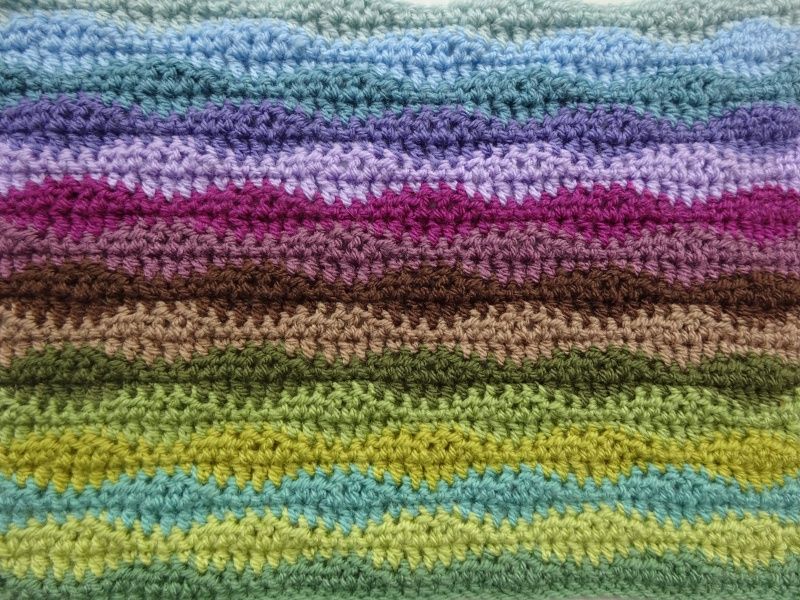 A striped crochet blanket in shades of green, blue, purple and brown.
