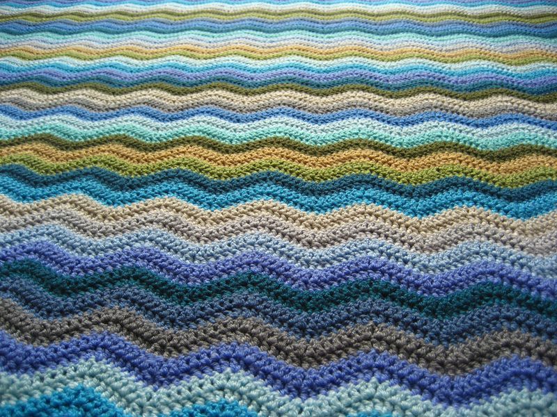 A close up of a crocheted ripple blanket in shades of blue, green, grey and brown.