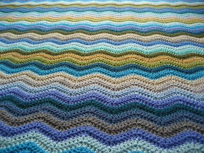 A close up of a crocheted ripple blanket in shades of blue, green, grey and brown.