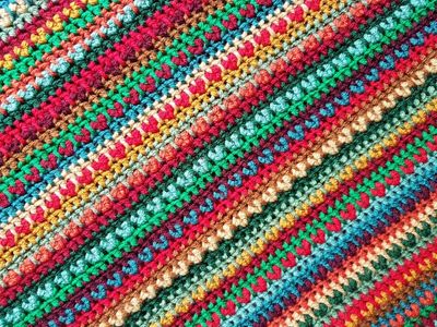 A close up of a striped crochet blanket in shades of green, red, blue and brown.