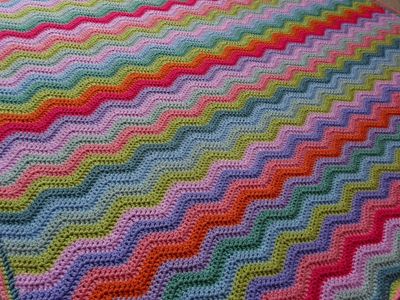 A close up of a ripple striped crochet blanket in shades of orange, green, blue, purple and pink.