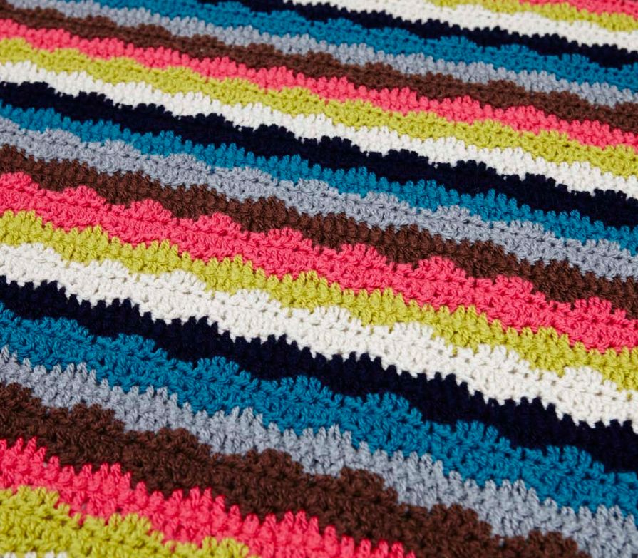 A crocheted blanket in stripes of navy, cream, green, blue, pink, brown and grey.
