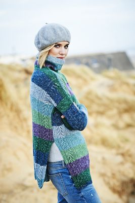 A woman is wearing a knitted sweater in a variegated blue, green an purple yarn.