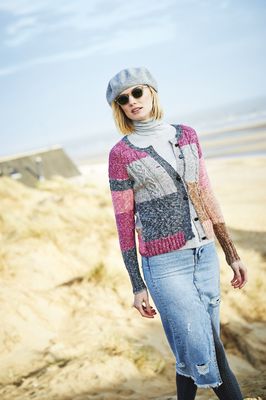 A woman is wearing a knitted cardigan in a variegated pink, grey, silver and brown yarn.