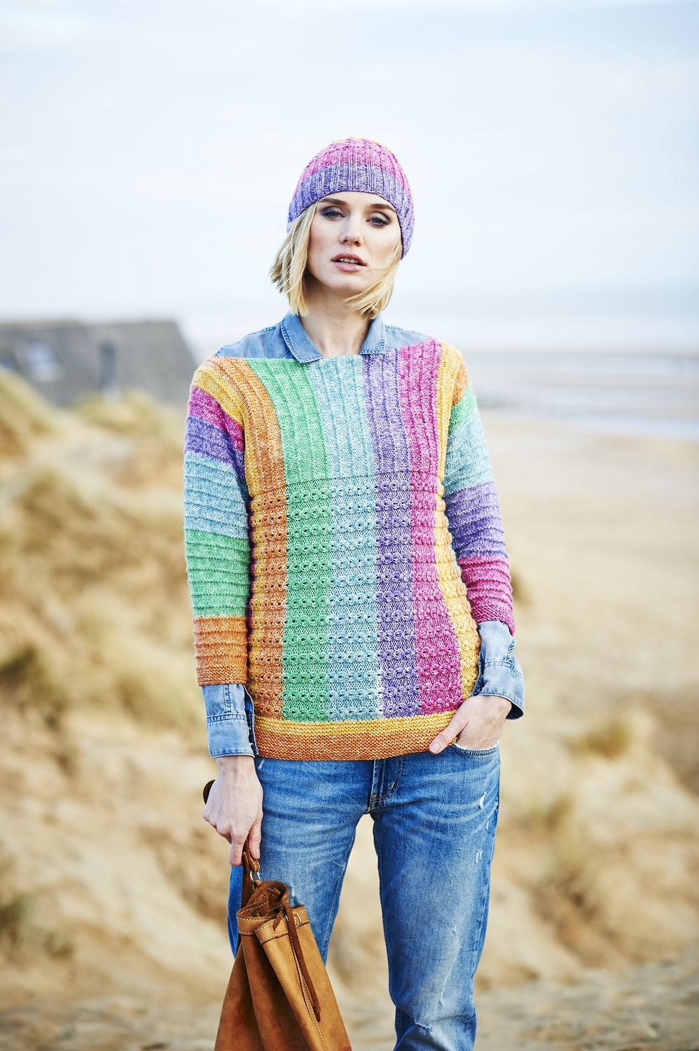 A woman is wearing a knitted sweater in a variegated green, yellow, pink, blue and purple yarn.