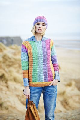 A woman is wearing a knitted sweater in a variegated green, yellow, pink, blue and purple yarn.