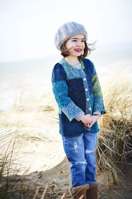 A girl is wearing a knitted cardigan in a variegated blue and green yarn.