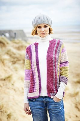 A woman is wearing a knitted cardigan in a variegated pink, purple, beige and green yarn.