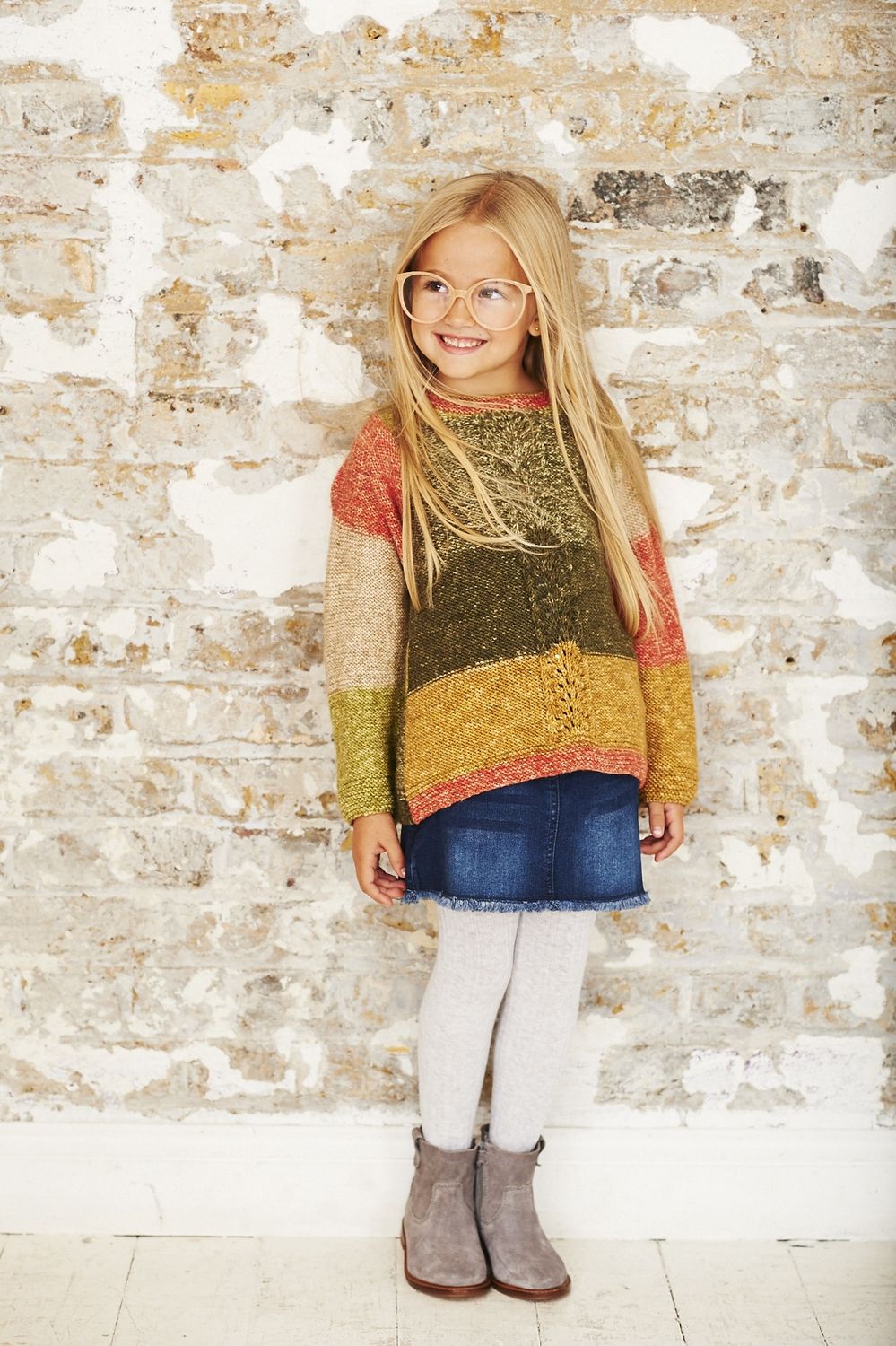 A girl is wearing a knitted sweater in a variegated green, yellow, coral and cream yarn.