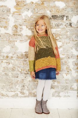 A girl is wearing a knitted sweater in a variegated green, yellow, coral and cream yarn.