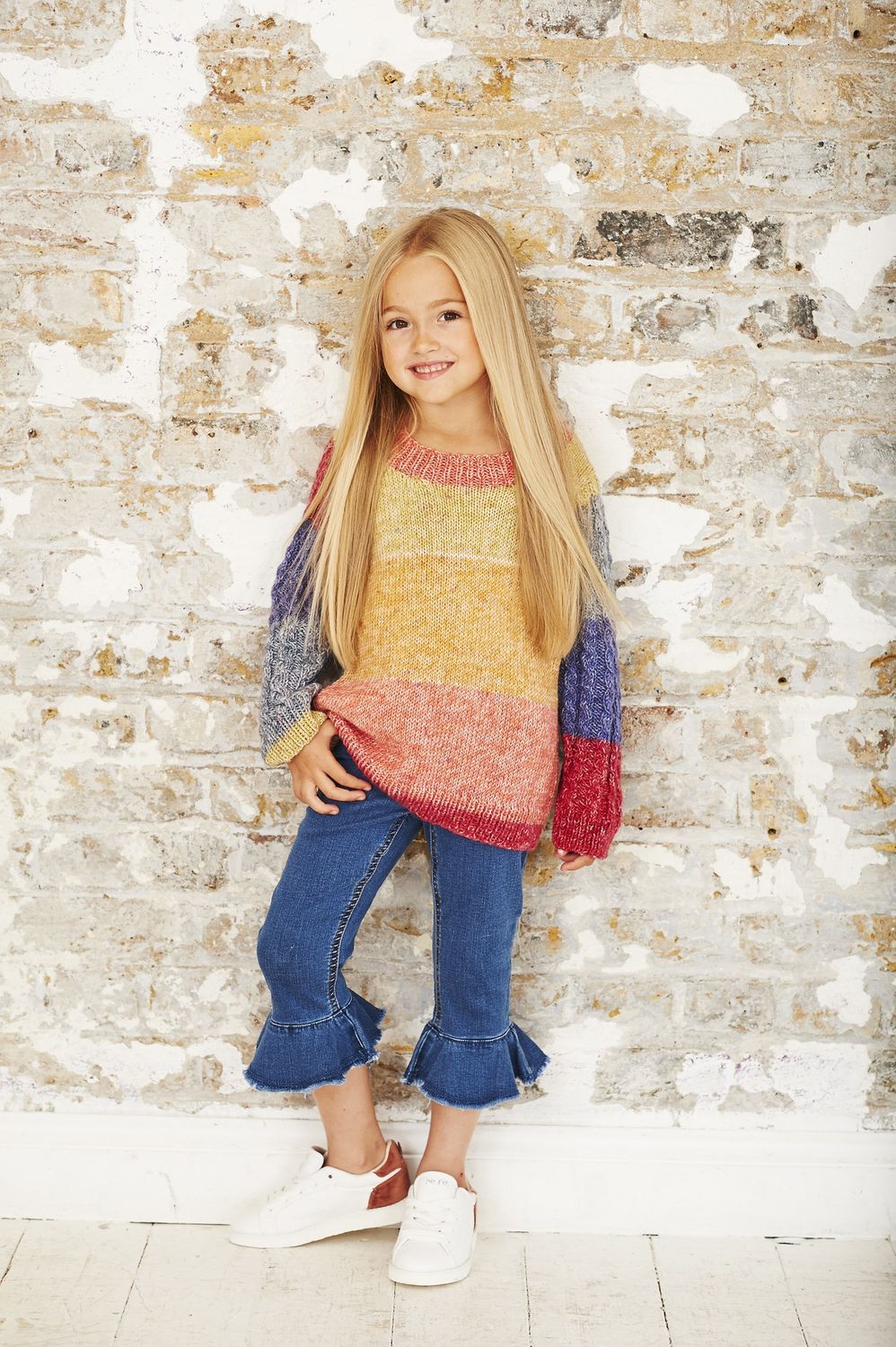 A girl is wearing a knitted sweater in a variegated red, coral, yellow, green and blue yarn.