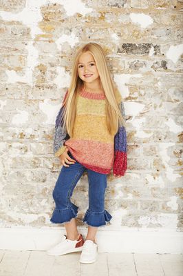 A girl is wearing a knitted sweater in a variegated red, coral, yellow, green and blue yarn.