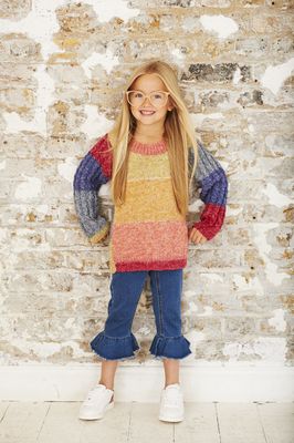A girl is wearing a knitted sweater in a variegated red, coral, yellow, green and blue yarn.