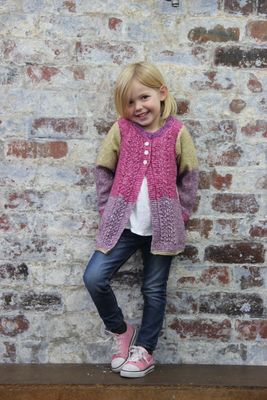 A girl is wearing a knitted cardigan in a variegated green, pink and purple yarn.