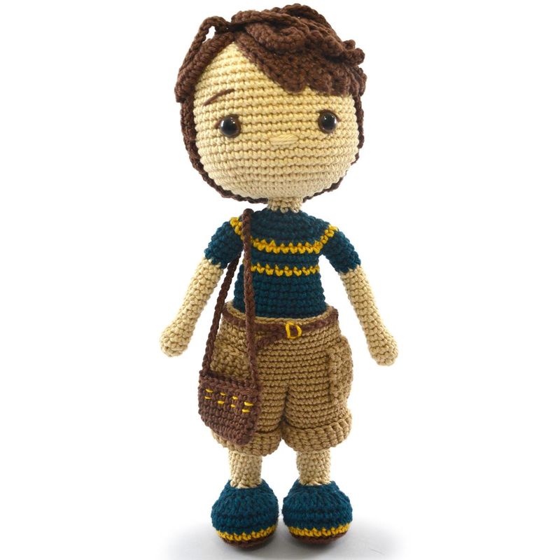 A crocheted doll, of a white boy with brown hair, a blue t-shirt, brown shorts and blue shoes.