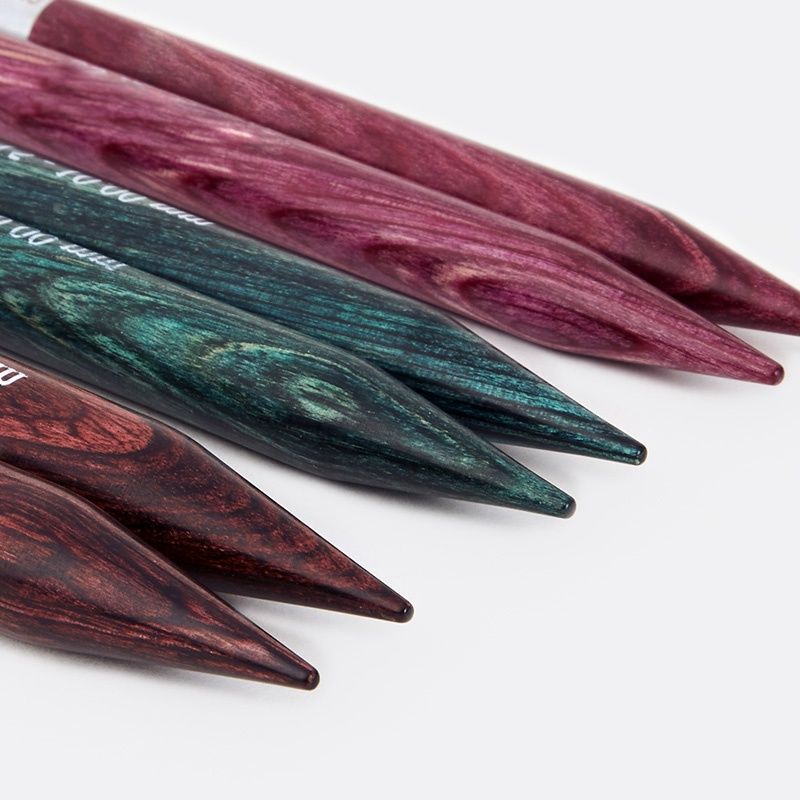 A close up of 3 pairs of wooden interchangeable knitting needles in various colours.