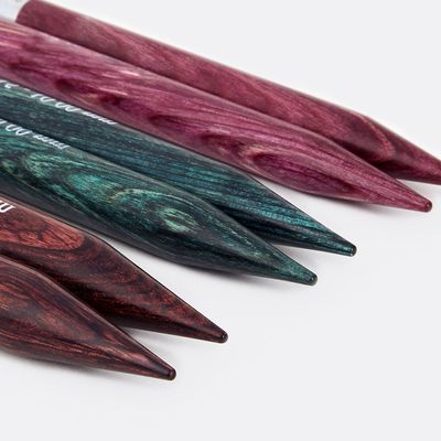 A close up of 3 pairs of wooden interchangeable knitting needles in various colours.