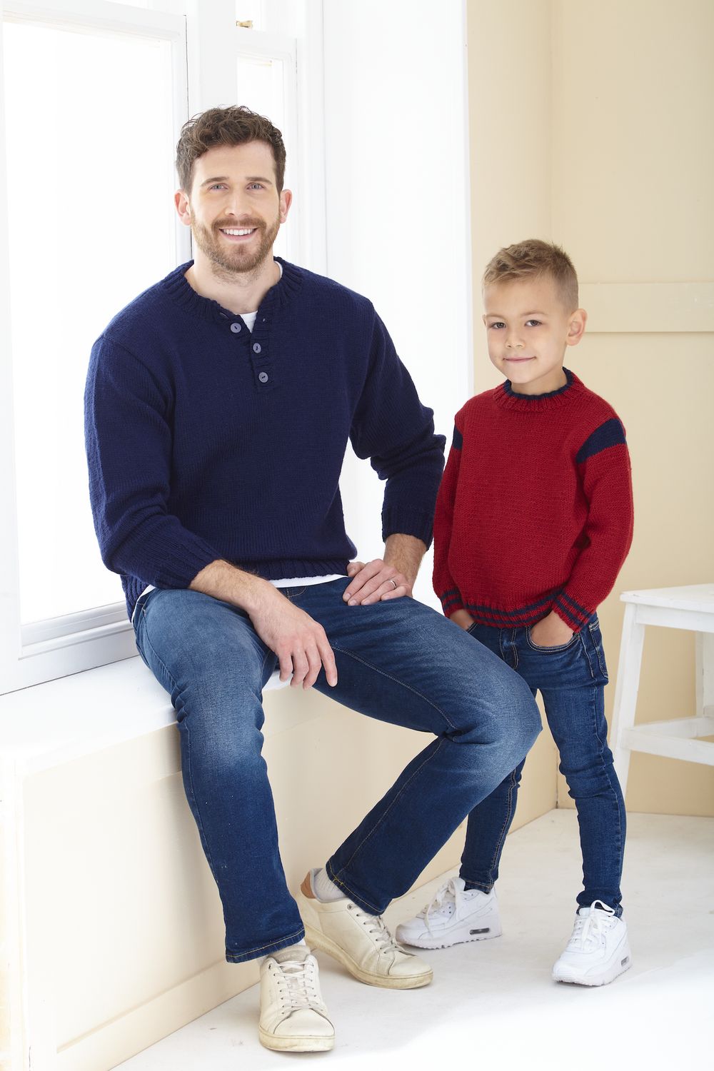 A man is wearing a navy blue knitted sweater and a boy is wearing a red knitted sweater.