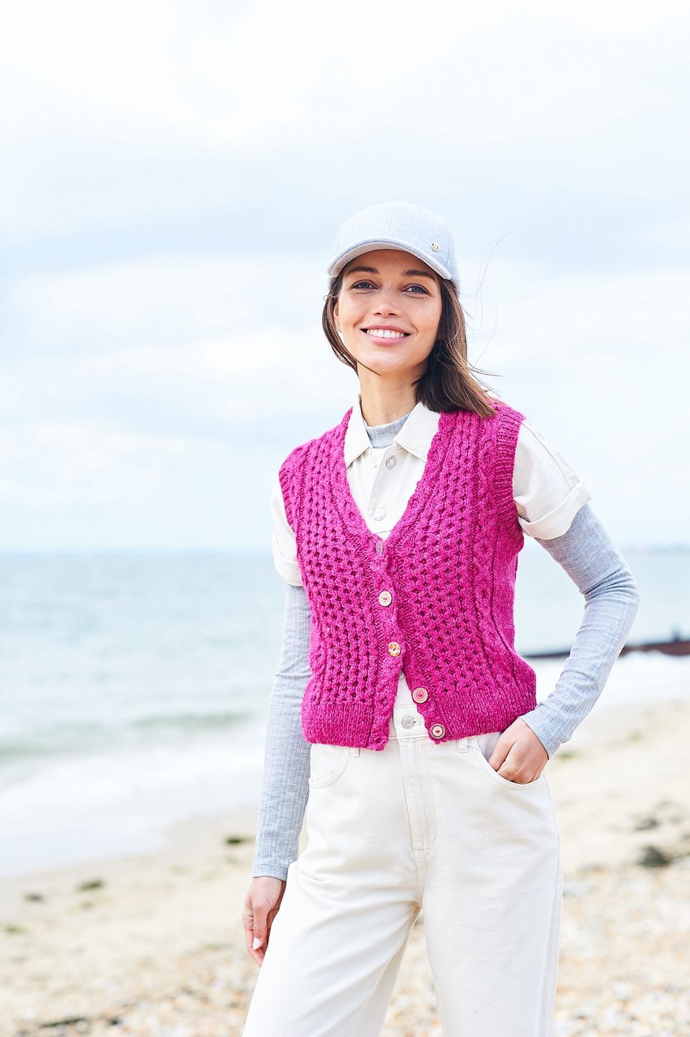 A woman is wearing a pink cable knit waistcoat.