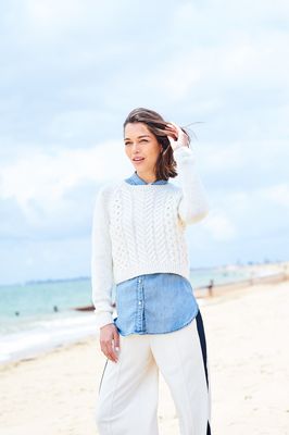 A woman is wearing a cream cable knit sweater.