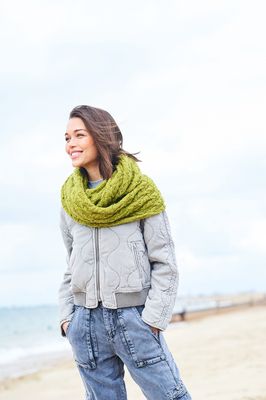 A woman is wearing a lime green cable knit cowl.