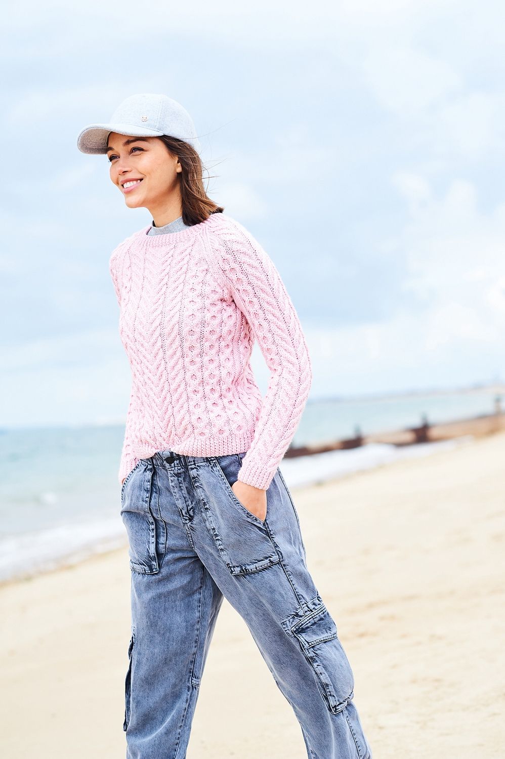 A woman is wearing a pale pink cable knit sweater.