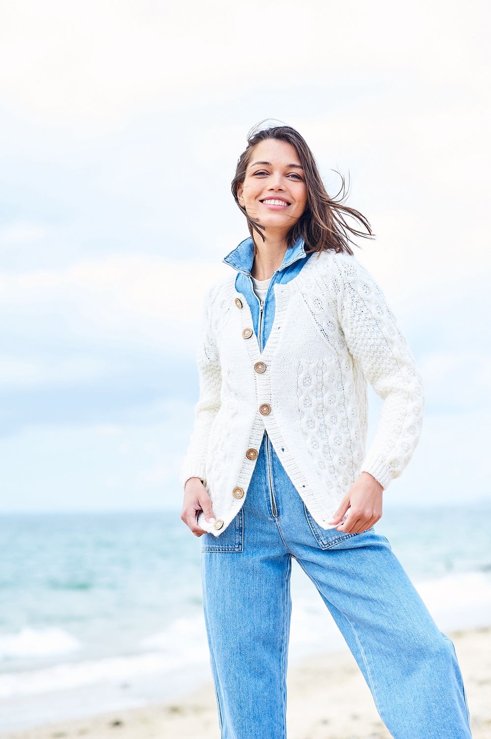 A woman is wearing a cream cable knit cardigan.