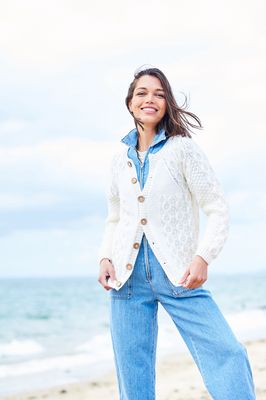 A woman is wearing a cream cable knit cardigan.