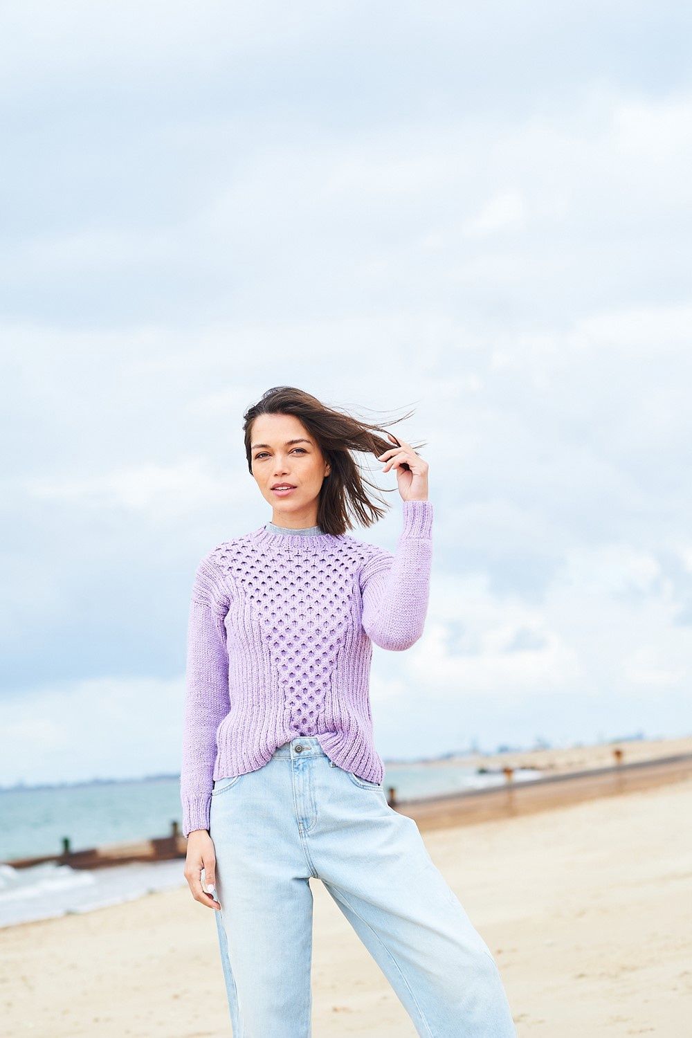 A woman is wearing a light purple cable knit sweater.