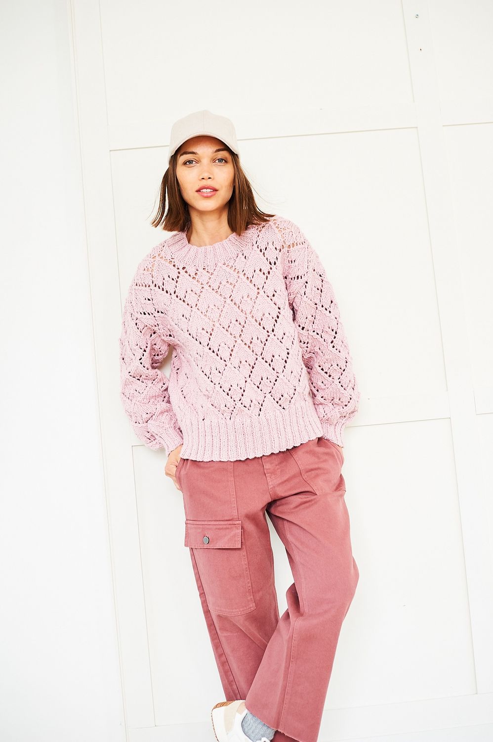 A woman is wearing a light blue knitted sweater with a diamond lace pattern.