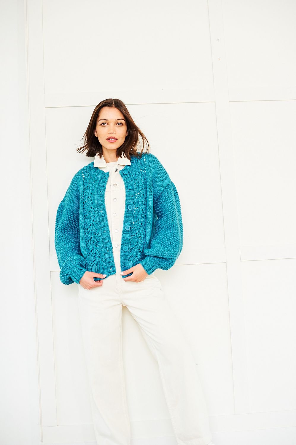 A woman is wearing a teal blue knitted cardigan with lace down the front.