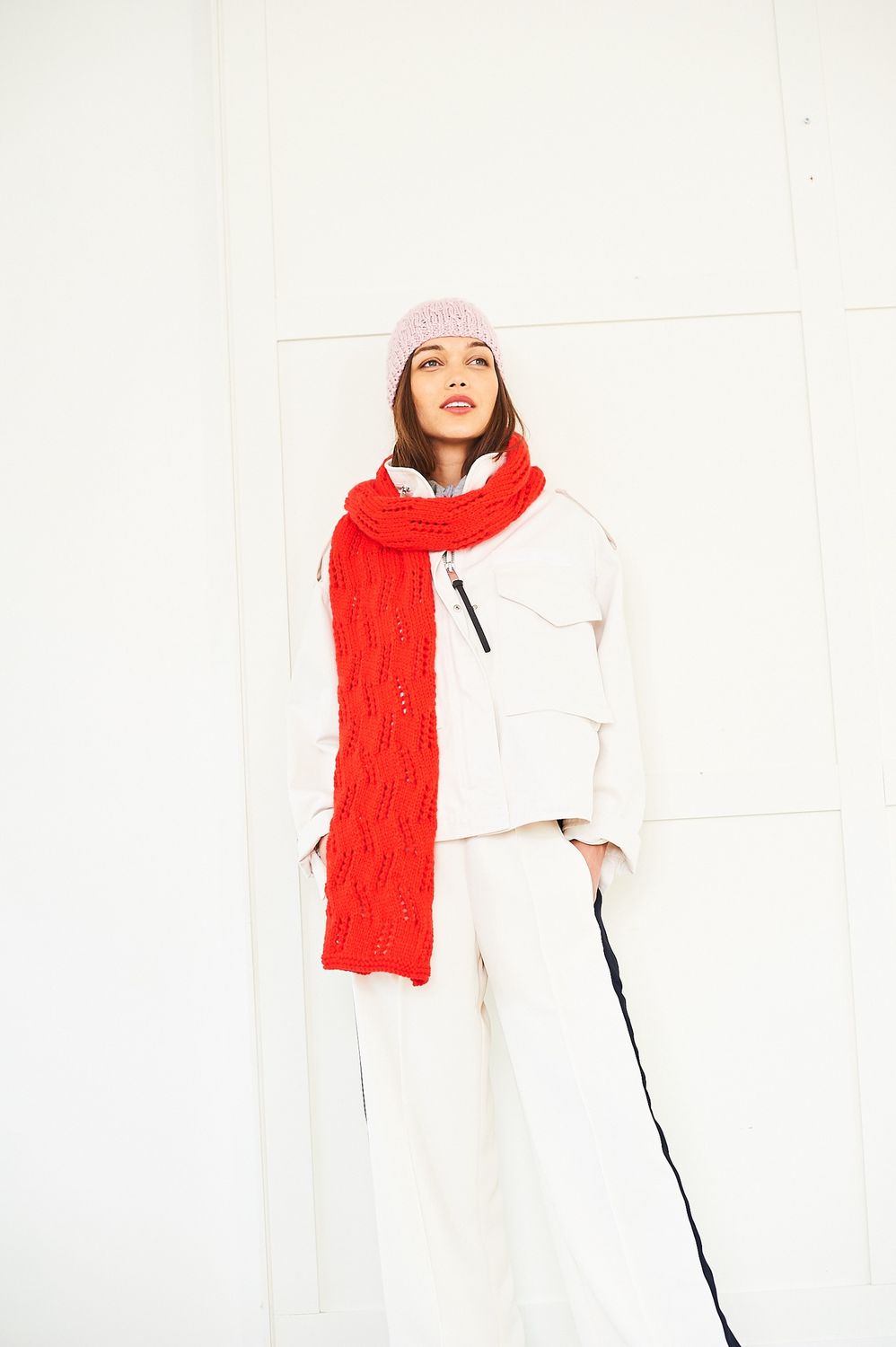 A woman is wearing a bright red lace knitted hat and light pink lace knitted hat.