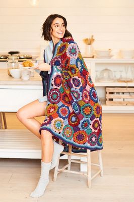 A woman has a green, red, blue, pink and purple crocheted blanket draped over her shoulders.