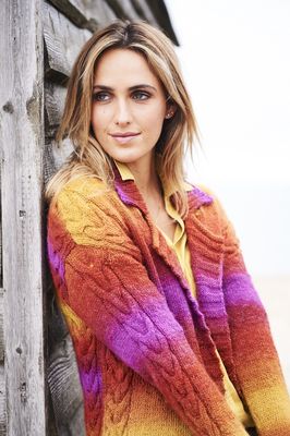 A woman is wearing a knitted cardigan in a variegated pink, orange and yellow yarn.